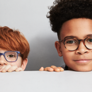 Two children wearing glasses peering over a wall